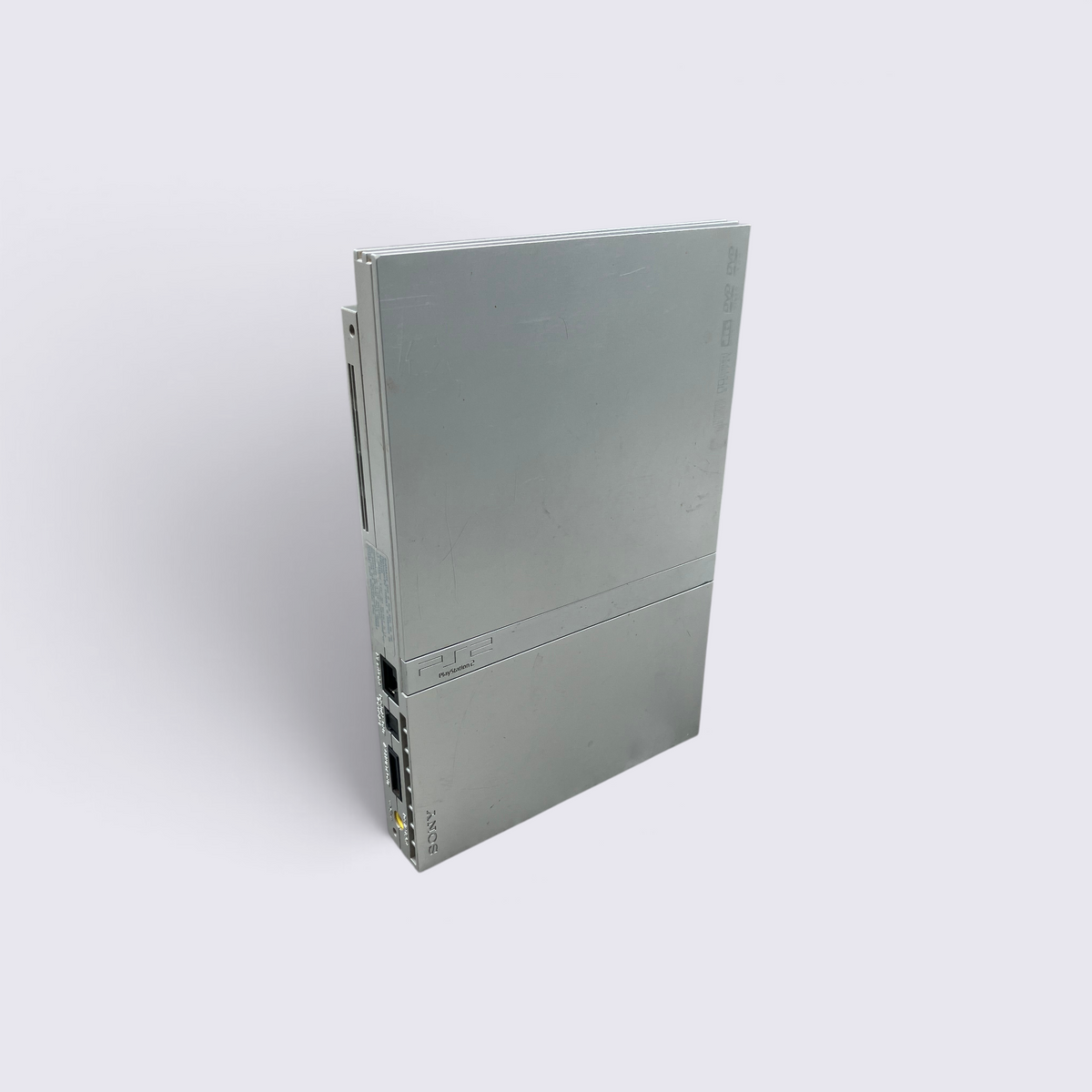 MrPixel silver PlayStation 2 Slim console standing vertically on a grey surface showing the front and side ports